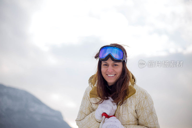 近景美丽的年轻女子在冬天的衣服站在一边，手拿木棍的背景雪山