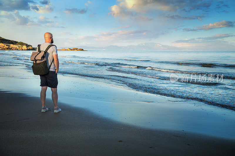 背着背包的旅行者在海边观看日出