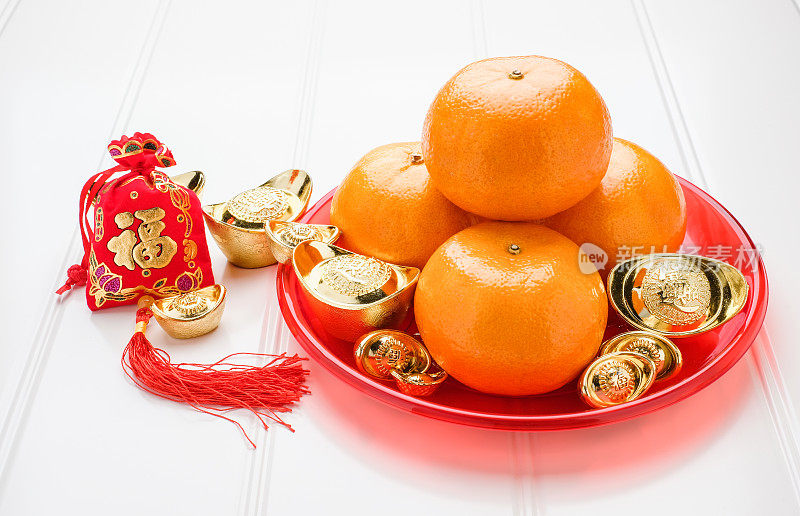 在中国的新年里，红色的毛毡布袋里装着金元宝和橘红色的橘子，红色的托盘放在白色的木头桌上，中文的意思是幸福，元宝意味着富有。