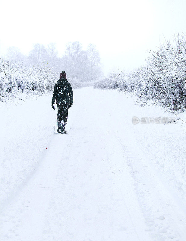 英国科茨沃尔德，格洛斯特郡，赛伦塞斯特公园，一个孤独的女人走在一条被雪覆盖的小路上