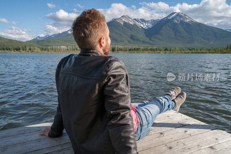 年轻男子坐在湖墩上凝视山景