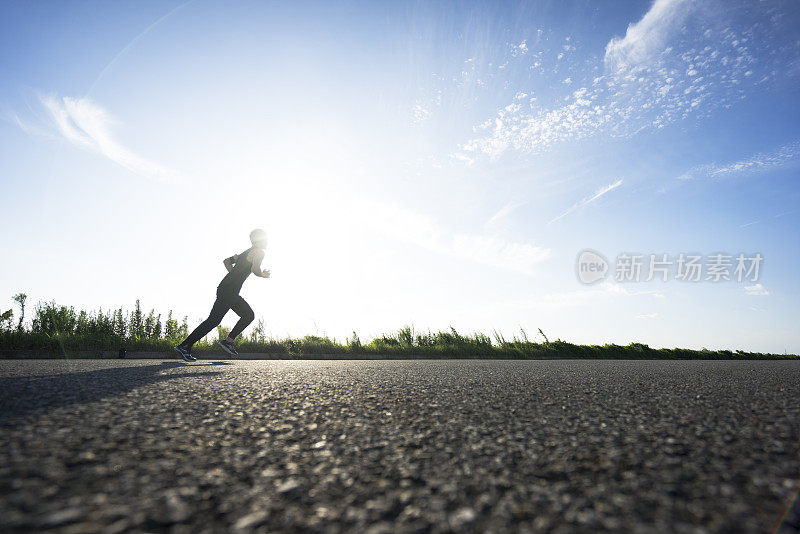 年轻的男运动员在柏油路上迎着天空奔跑