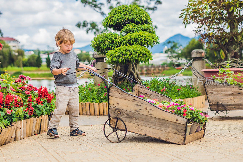孩子推着手推车在花园里。可爱的蹒跚学步的小男孩在后院玩手推车。一个孩子在户外拖着玩具车