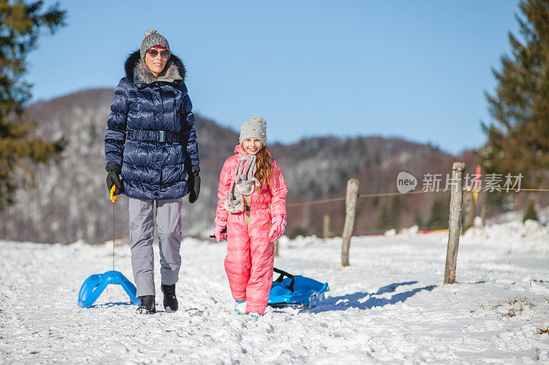 微笑的母亲和女儿拉雪橇和走在雪地上