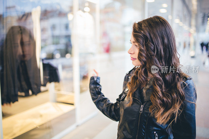 美丽时尚的女孩走在城市里，看着商店的橱窗。
