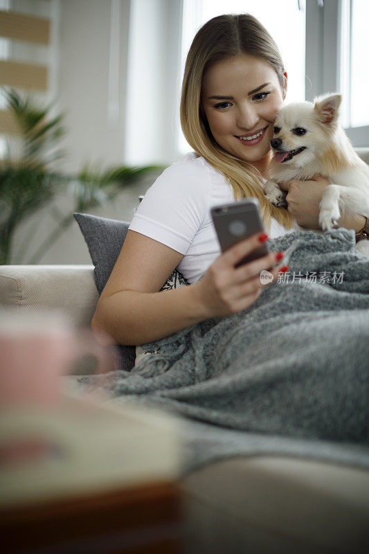 年轻女子和她的狗在家里使用手机