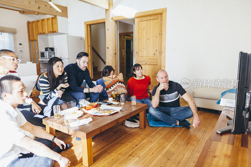 一群不同民族的朋友在家里喝着啤酒和披萨看电影