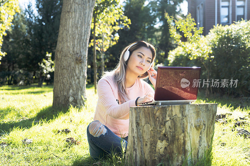 亚洲视频博主女人在后院用耳机在笔记本电脑上广播