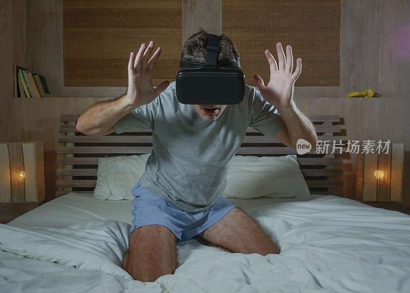 年轻兴奋和惊奇的男人戴着VR虚拟现实眼镜设备玩互联网3D模拟游戏，享受刺激和震撼的视觉体验在家里的床上