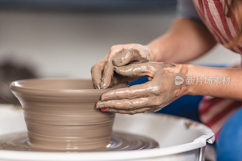 在艺术工作室里，女性的双手在陶轮上制作陶器