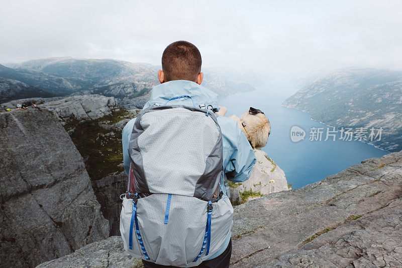 一名背包客带着狗在挪威的布道石上看着吕瑟峡湾