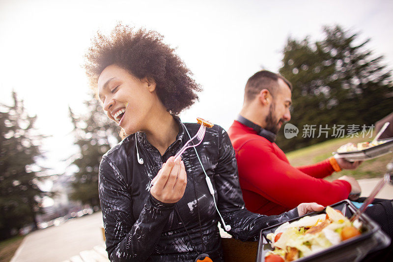 一对年轻夫妇在公园的长椅上邻座，吃着蛋白质沙拉