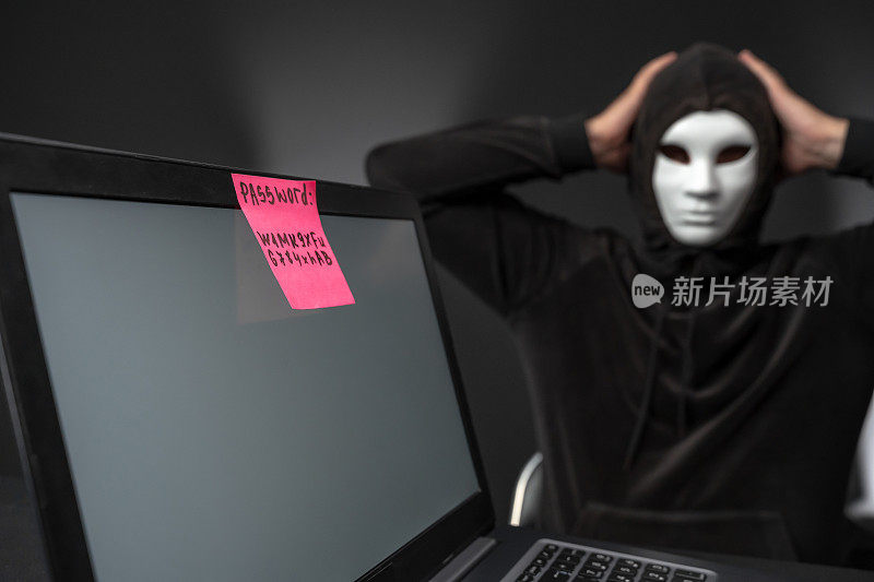 蒙面黑客把头藏在笔记本电脑后面，电脑上有强密码