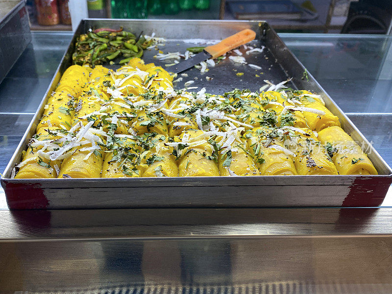 印度商店陈列的Khandvi(辣克面粉卷)的托盘图像，高架视图，关注前景