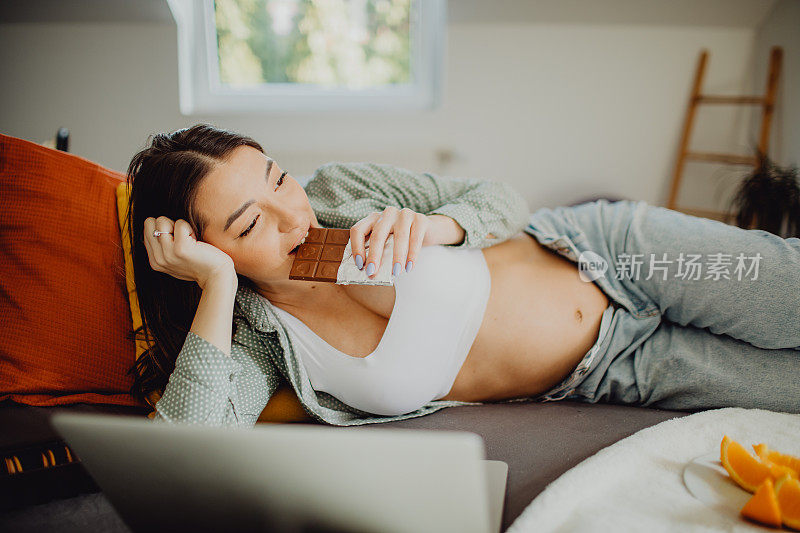 年轻的孕妇在床上吃巧克力放松