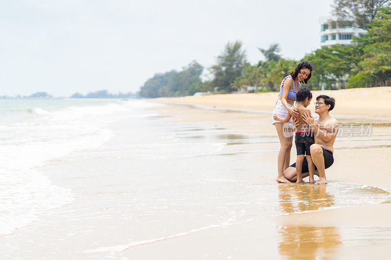 暑假，一对亚洲父母带着小儿子一起在热带海滩上玩海。
