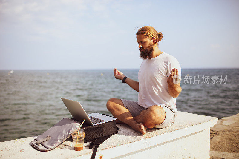 数码游民坐在沙滩上，拿着笔记本电脑在岸边沉思
