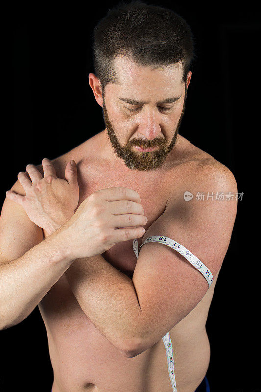 男人用卷尺测量他的手臂二头肌，看肌肉增加或体重减少的体脂百分比