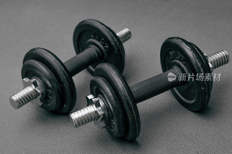 健身背景。两个10公斤重的哑铃放在灰色垫子上。运动概念:灰色垫子，两个10公斤重的黑色哑铃