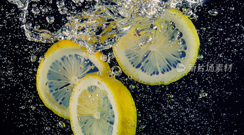 水下鲜榨的甜柠檬水，生柠檬片落在苏打水中，深蓝色或黑色的背景。近景柠檬水或高球柠檬鸡尾酒清凉饮料