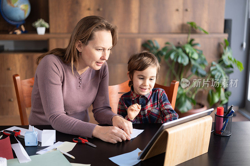 孩子男孩和母亲做折纸玩具使用彩色纸的步骤，按照指导的视频教程在数字平板电脑上