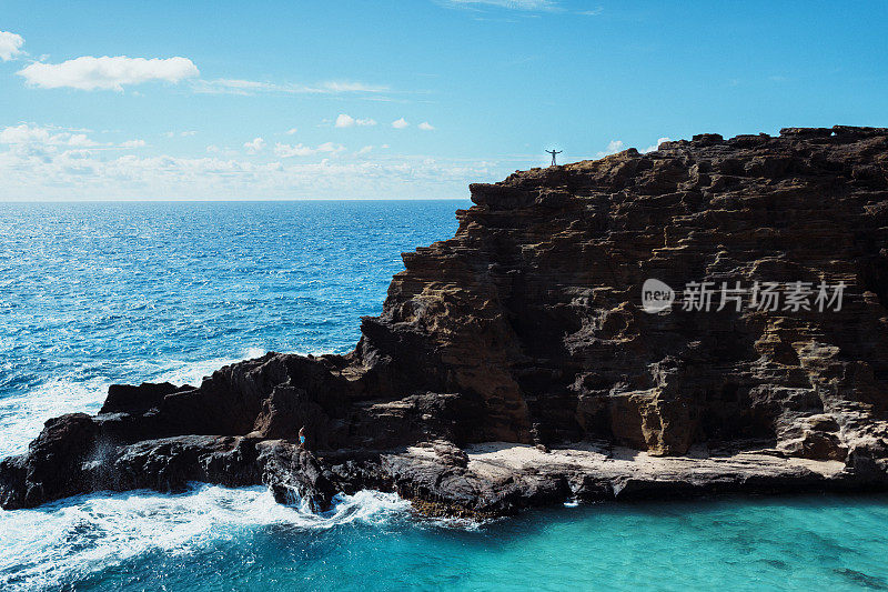 宽镜头的男子举起手臂，在悬崖上与海景