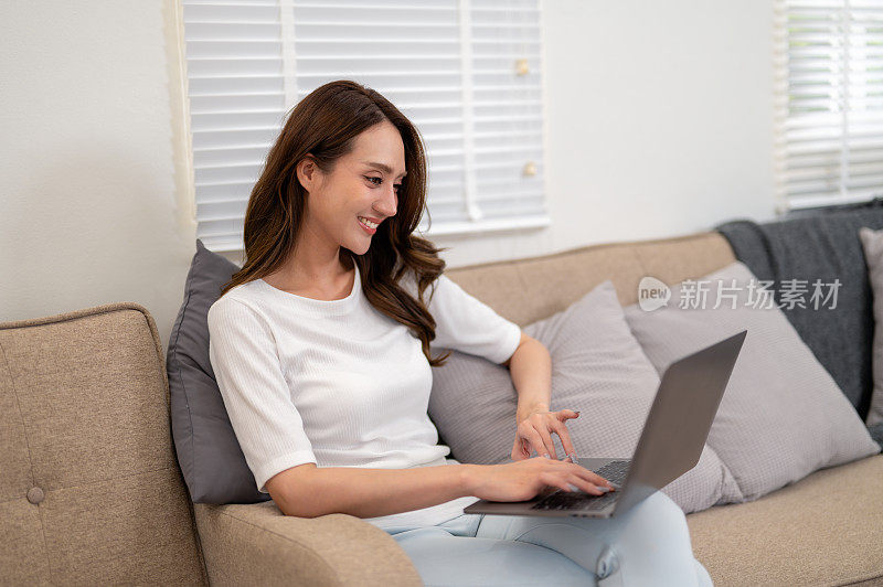 一位年轻女子懒洋洋地躺在家里的沙发上，舒舒服服地使用着她的笔记本电脑，享受着悠闲的一天。