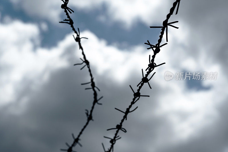黑色的铁丝网在戏剧性的灰色蓝天背景下，囚禁，监狱或监狱，劳工或集中营的抽象概念，没有人。边缘锋利的旧倒刺铁丝，缺乏自由，栅栏