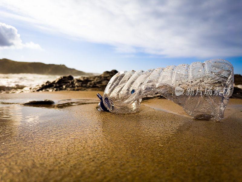 在葡萄牙的沙滩上，一个装满垃圾的空塑料瓶被疏忽地遗忘在沙滩上