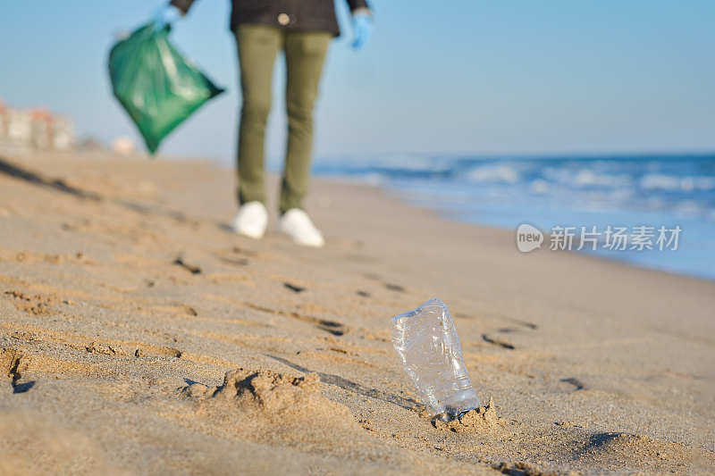 在一个阳光明媚的日子里，地中海海滩上，一个塑料瓶里的水和一个负责收集废物的白种X一代男性的特写镜头