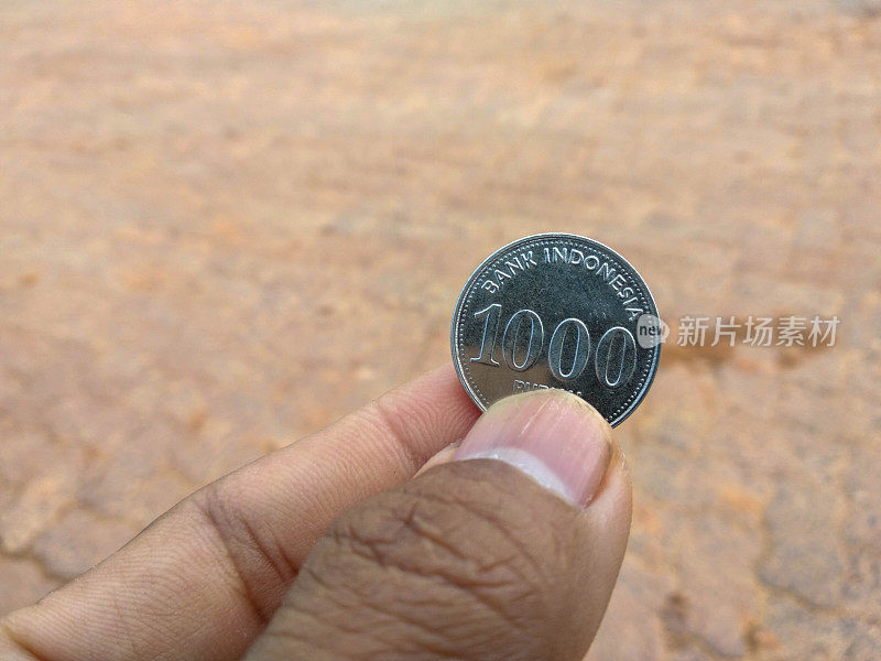 拿着一枚刻有1000印尼盾的硬币