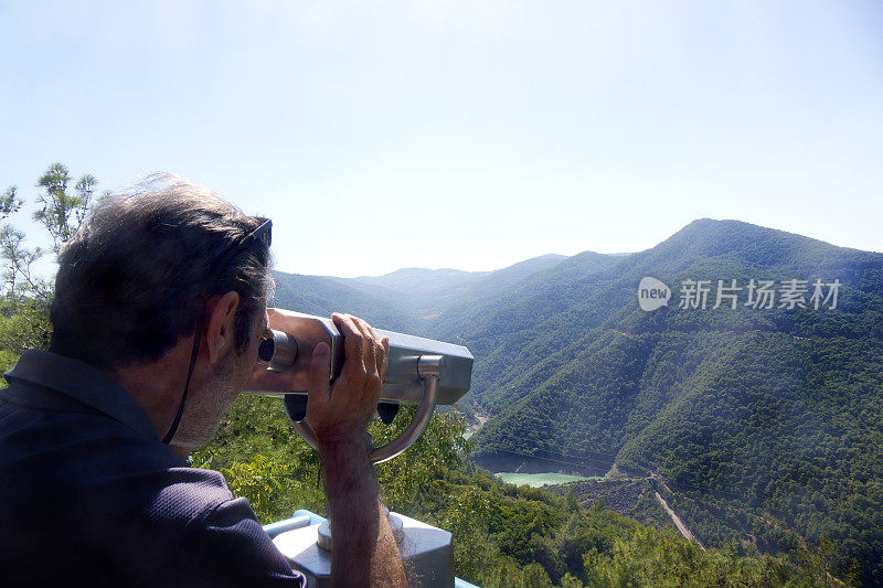 中年男子用投币操作的双筒望远镜看风景