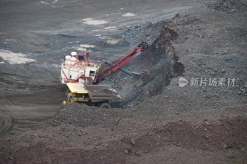 挖土机正在挖掘铁矿石，准备运送到卡车上