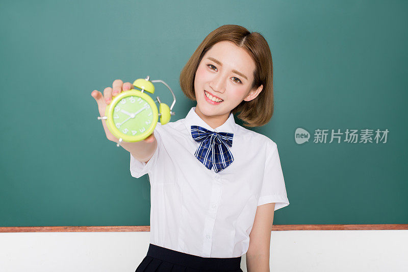 一个十几岁的中国女孩在黑板前拿着闹钟的肖像