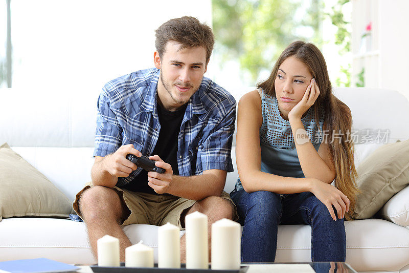 男人在玩电子游戏，女朋友在旁边无聊