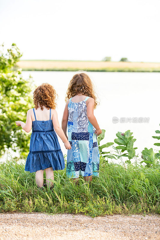 两个年轻女孩站在湖上的后视图