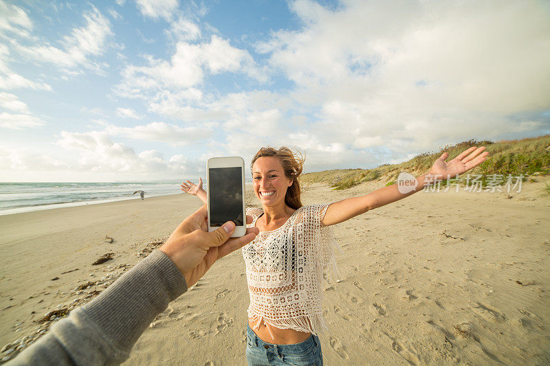 日落时分，一名男子用手机在海滩上捕捉女友