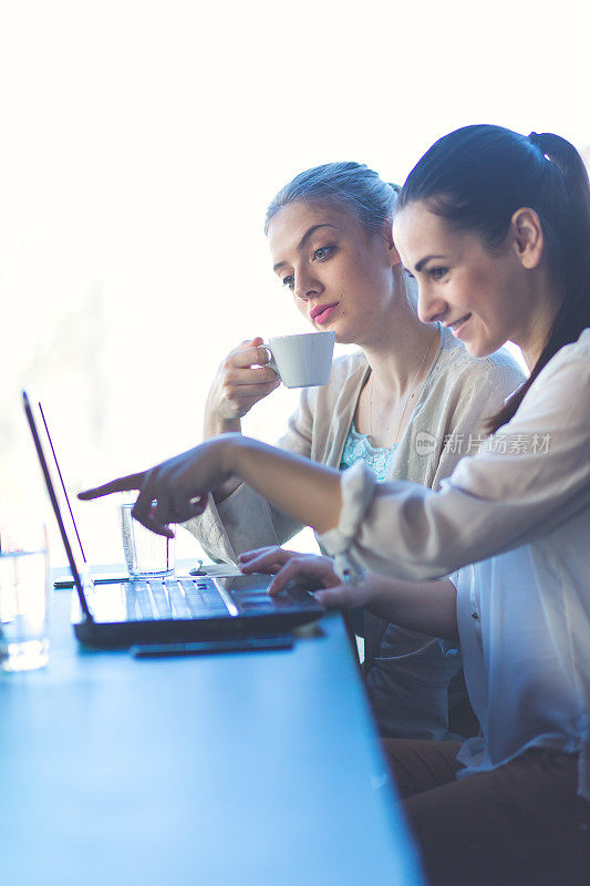 年轻女性喝着咖啡，在咖啡馆聊天，用笔记本电脑工作，浏览互联网