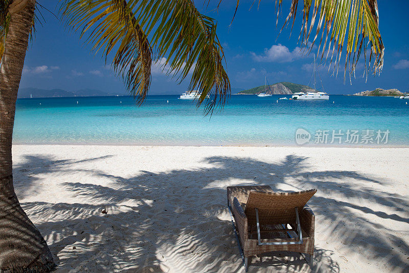 在美丽的热带海滩上，棕榈树下的躺椅