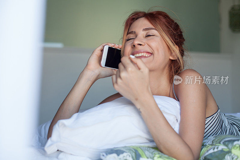 一张年轻女子躺在床上用智能手机的照片