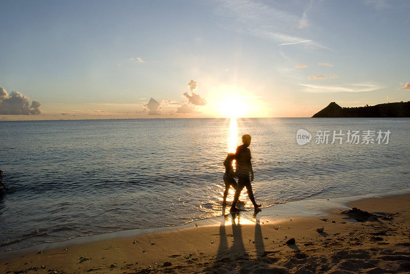 夕阳下一对情侣在海滩上散步的剪影