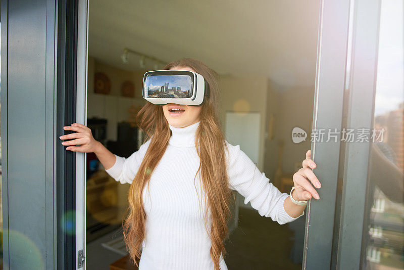 年轻漂亮的女人戴着虚拟现实眼镜在阳台上