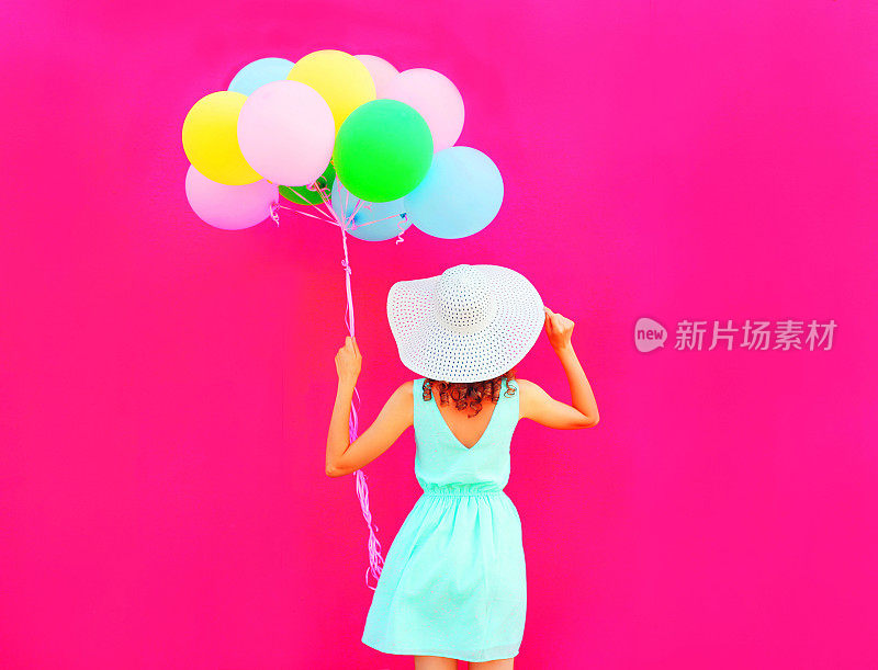 快乐的女人拿着一个空气彩色的气球在粉红色的背景上玩得很开心
