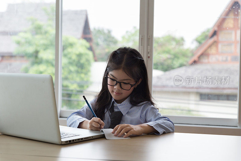 美丽的女学生在网上学习，学习，在家里的书桌上写笔记