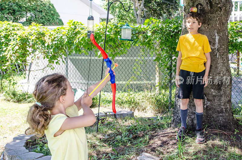 夏日里，一个小女孩拿着弓箭瞄准哥哥头上的苹果