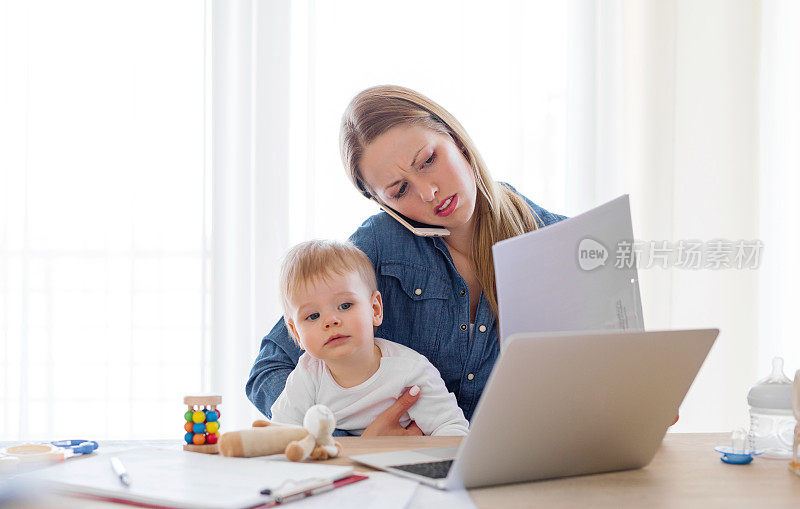 母亲抱着孩子在家用电脑工作