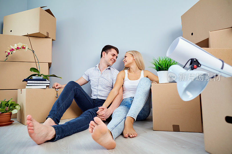 一对年轻夫妇坐在一栋新公寓的地板上。