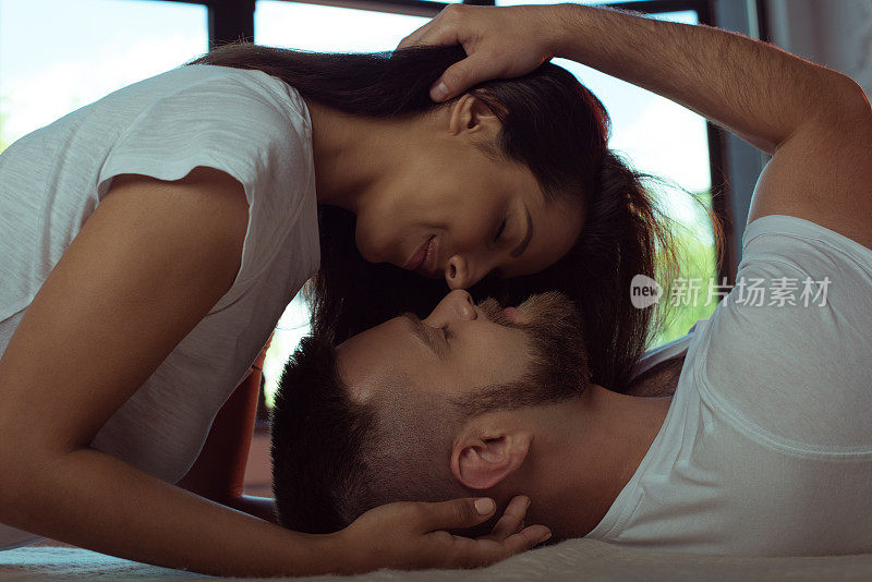 温柔的年轻夫妇闭着眼睛在床上拥抱亲吻