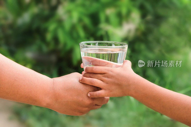 女人用双手喝水，孩子用双手绿叶作背景