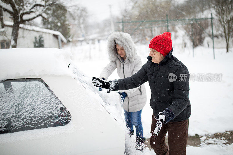 一位妇女正在清理一辆被雪覆盖的汽车。在大雪堆周围